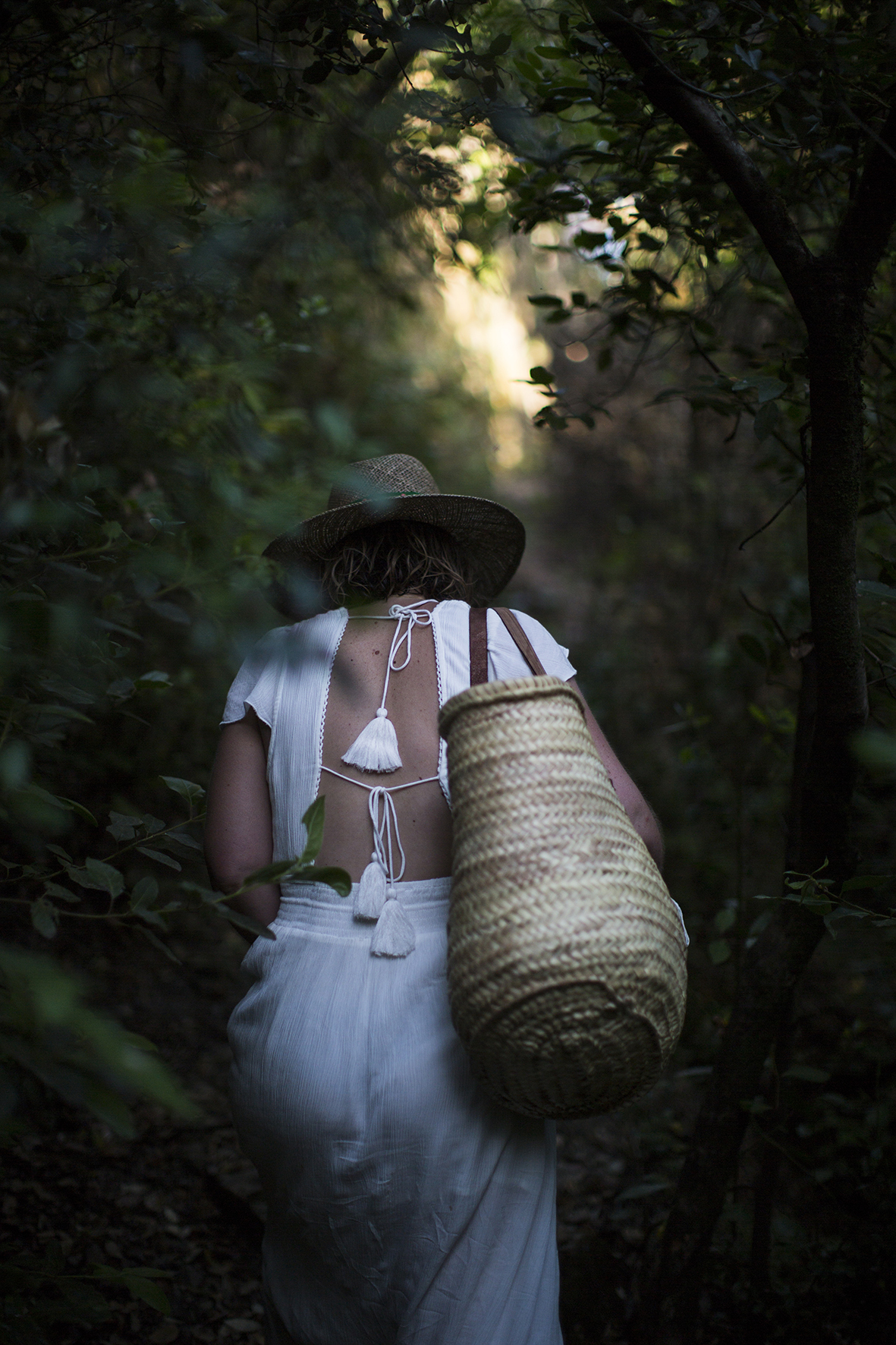 Femme artiste de dos, avec un panier, dans un chemin forestier touffu